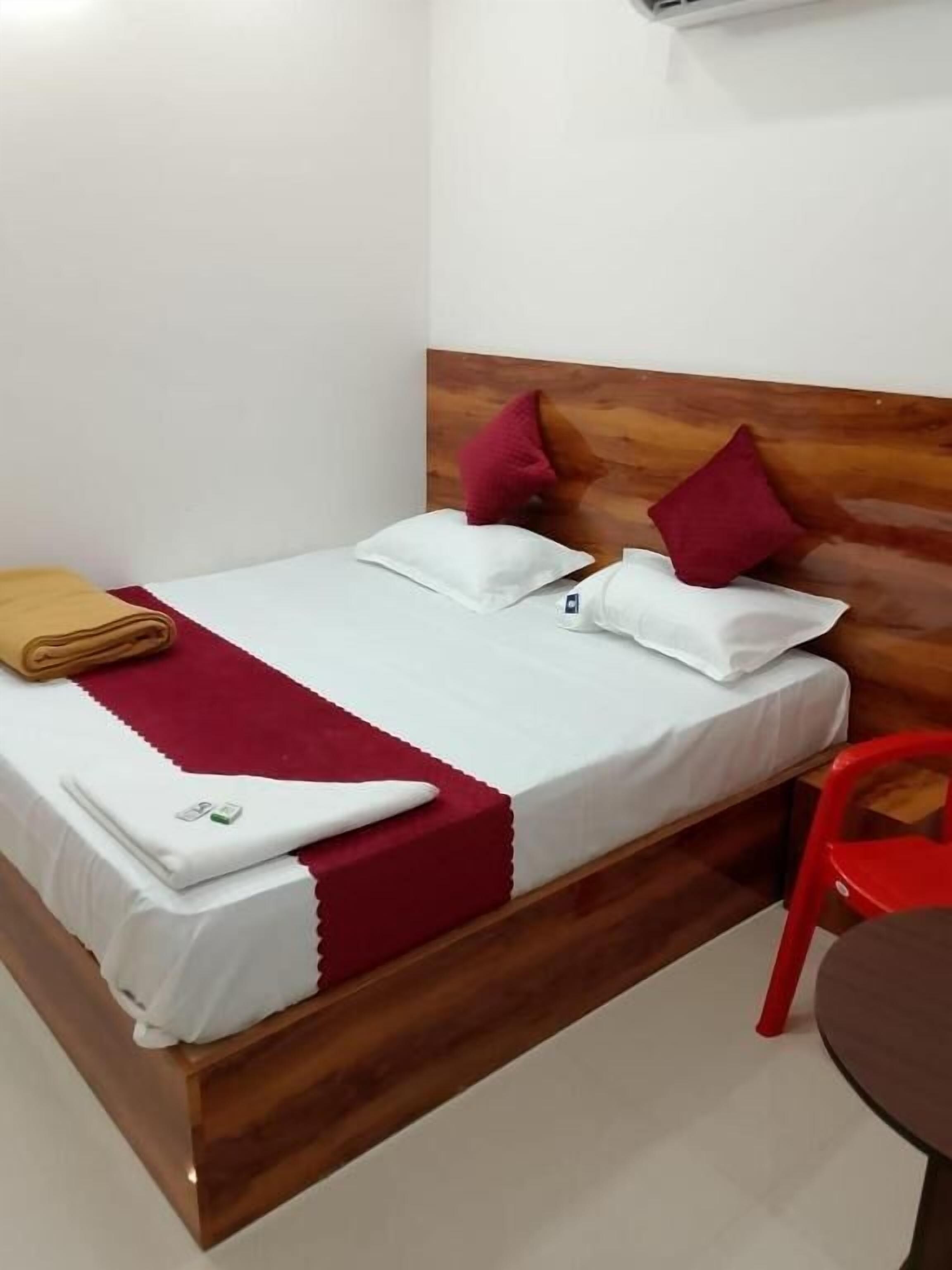 Una cama individual con cabecera de madera, ropa de cama blanca y detalles en rojo.