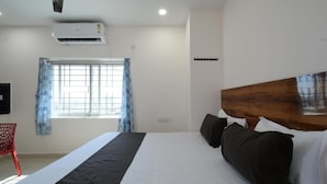 Une chambre d’hôtel avec un lit, une fenêtre avec des rideaux, un ventilateur de plafond et un appareil de climatisation.