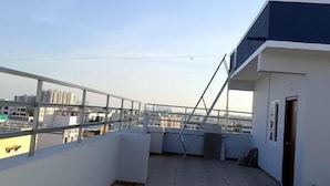 Une terrasse sur le toit, ouverte et offrant une vue dégagée sur les toits de la ville, avec une rambarde en métal et une porte située à droite.