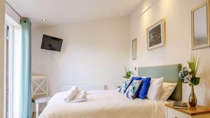 Quarto de hotel com cama, mesa de cabeceira, televisão na parede e janela com cortinas.