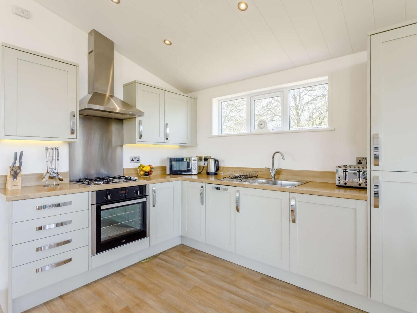 A modern kitchen with white cabinets, a stainless steel range hood, a built-in oven, a microwave, a toaster, and a sink.