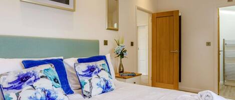 A hotel room with a bed, pillows, a vase with flowers, a wooden door, and a towel rack.