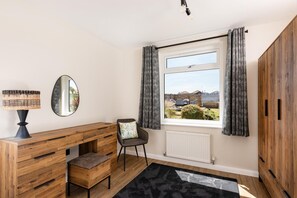 A room with a wooden desk, a chair, a mirror, a window with curtains, and a view of the outside. - 1 Bed in Norwich (oc-82230) (Mundesley)