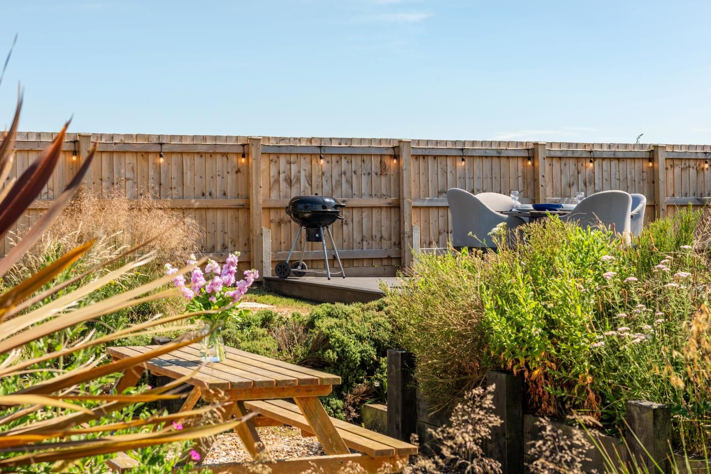 Ein Garten mit Holzzaun, Grill, Gartenmöbeln und verschiedenen Pflanzen.
