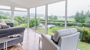 Ein geräumiges Zimmer mit großen Fenstern, einem grauen Sofa und Holzboden.