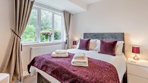 Ein Schlafzimmer mit einem Bett, einem Fenster mit Vorhängen, einem Heizkörper und einer Nachttischlampe.