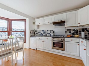 A modern kitchen with white cabinetry, a gas stove, an oven, and a view through a large window. - 3 Bed in Ilfracombe (oc-82274) (Ilfracombe)