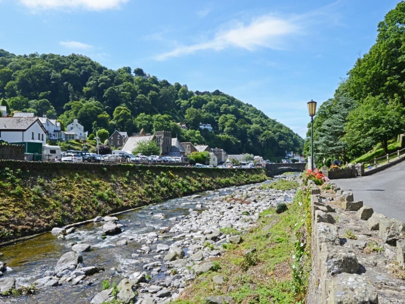 Une rivière bordée de rochers, un mur de pierres et des bâtiments sur la rive opposée.