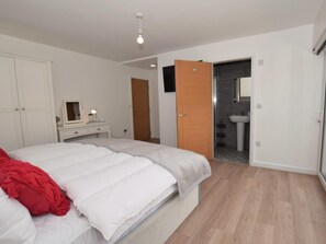 Ein Schlafzimmer mit Bett, Schminktisch, Spiegel und einem durchgehenden Türrahmen sichtbaren Badezimmer.