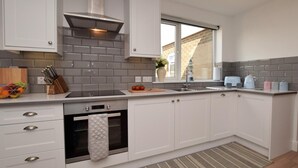 A modern kitchen with white cabinetry, a built-in oven, a stainless steel range hood, a window, and a striped rug. - 4 Bed in Chathill (oc-82235) (Beadnell)