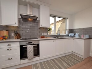 Eine moderne Küche mit weißen Schränken, einem eingebauten Backofen, einer Edelstahl-Dunstabzugshaube, einem Fenster und einem Streifen Teppich.