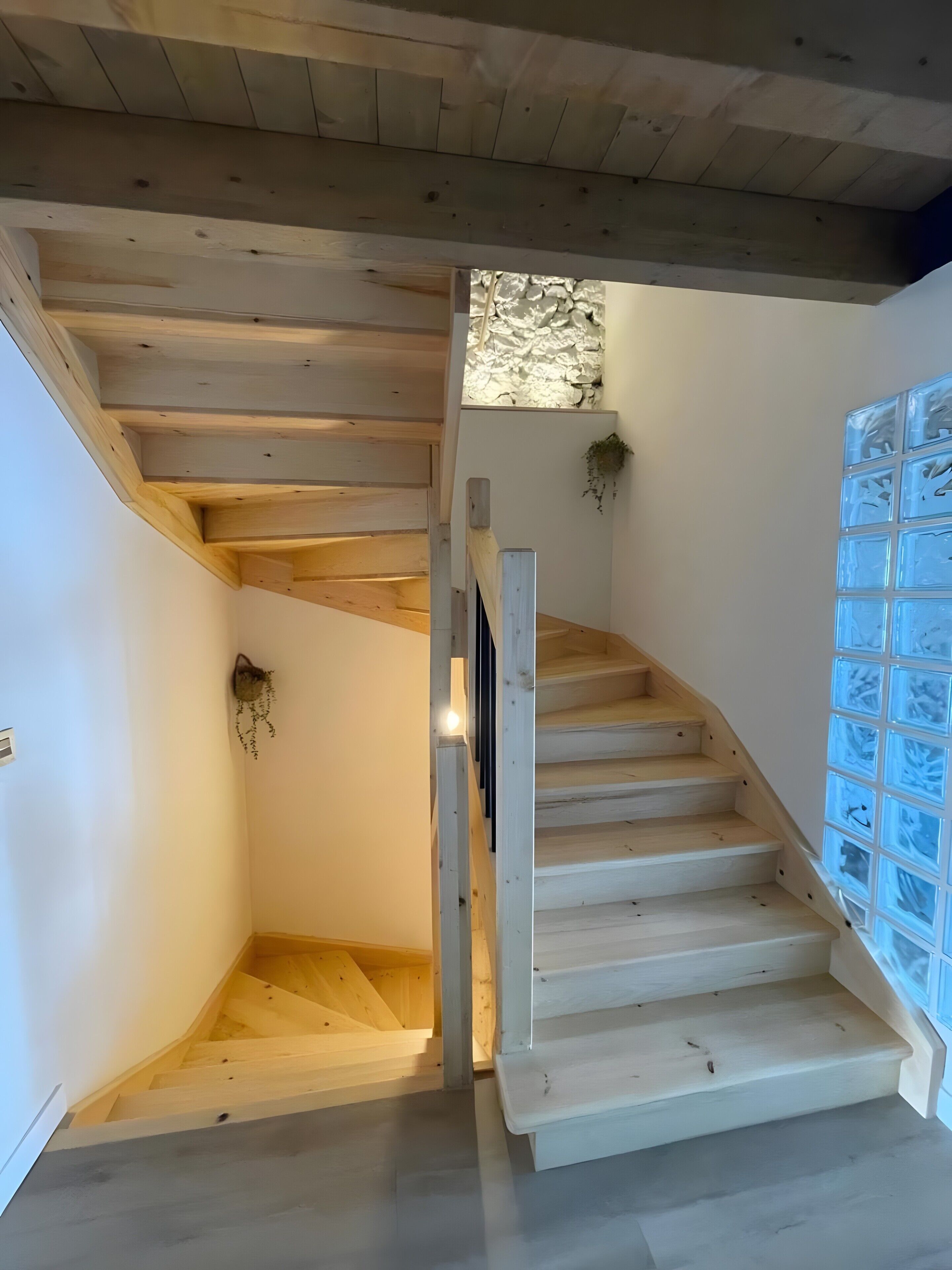 Una escalera de madera con un muro de bloques de vidrio a un lado.