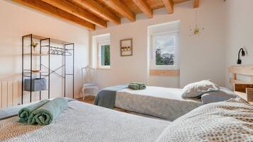 Una habitación con dos camas, techo de madera, ventana con vistas y una estantería metálica con ropa.