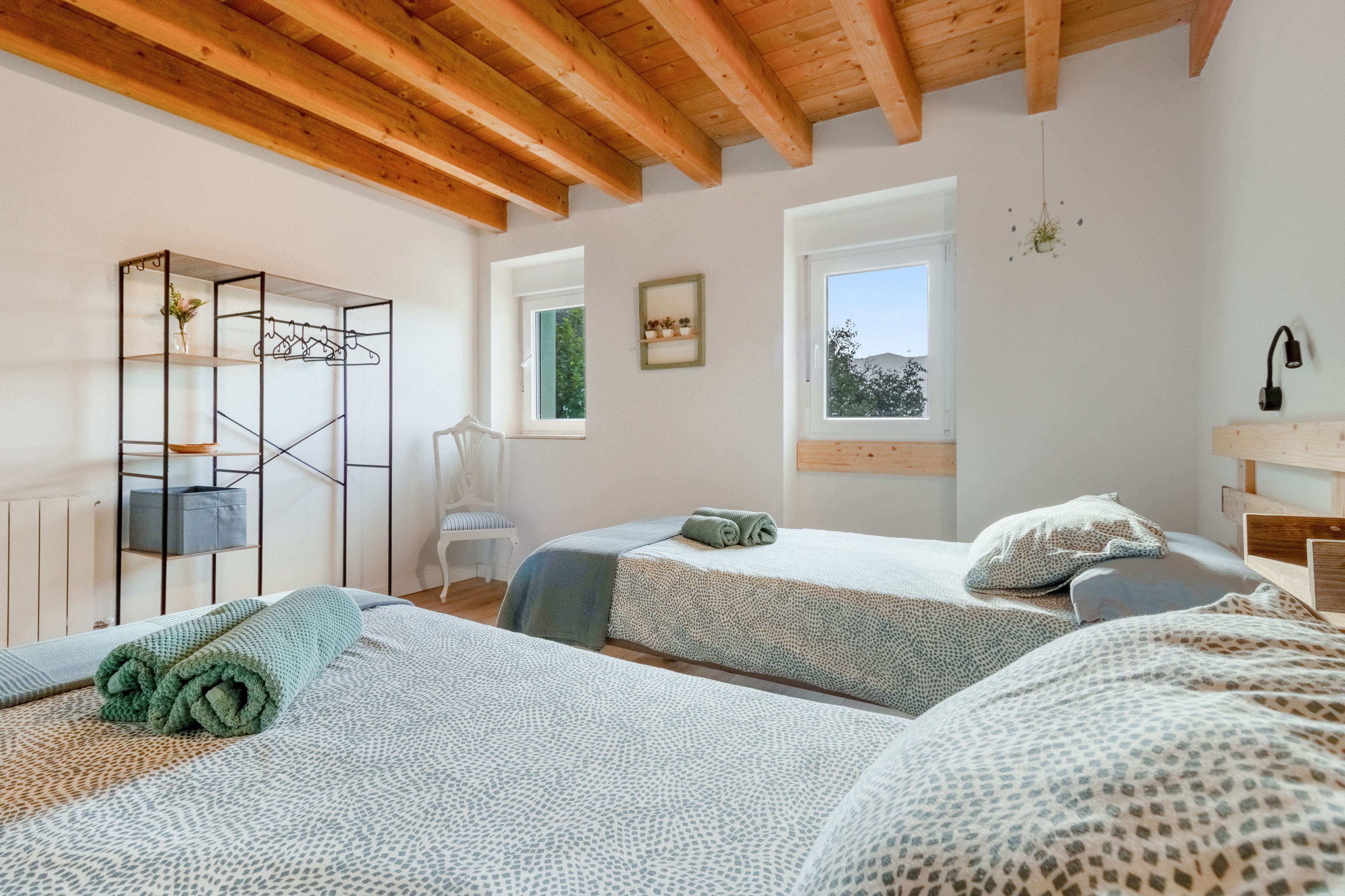 Een slaapkamer met twee bedden, een houten plafond, een raam en een stoel.