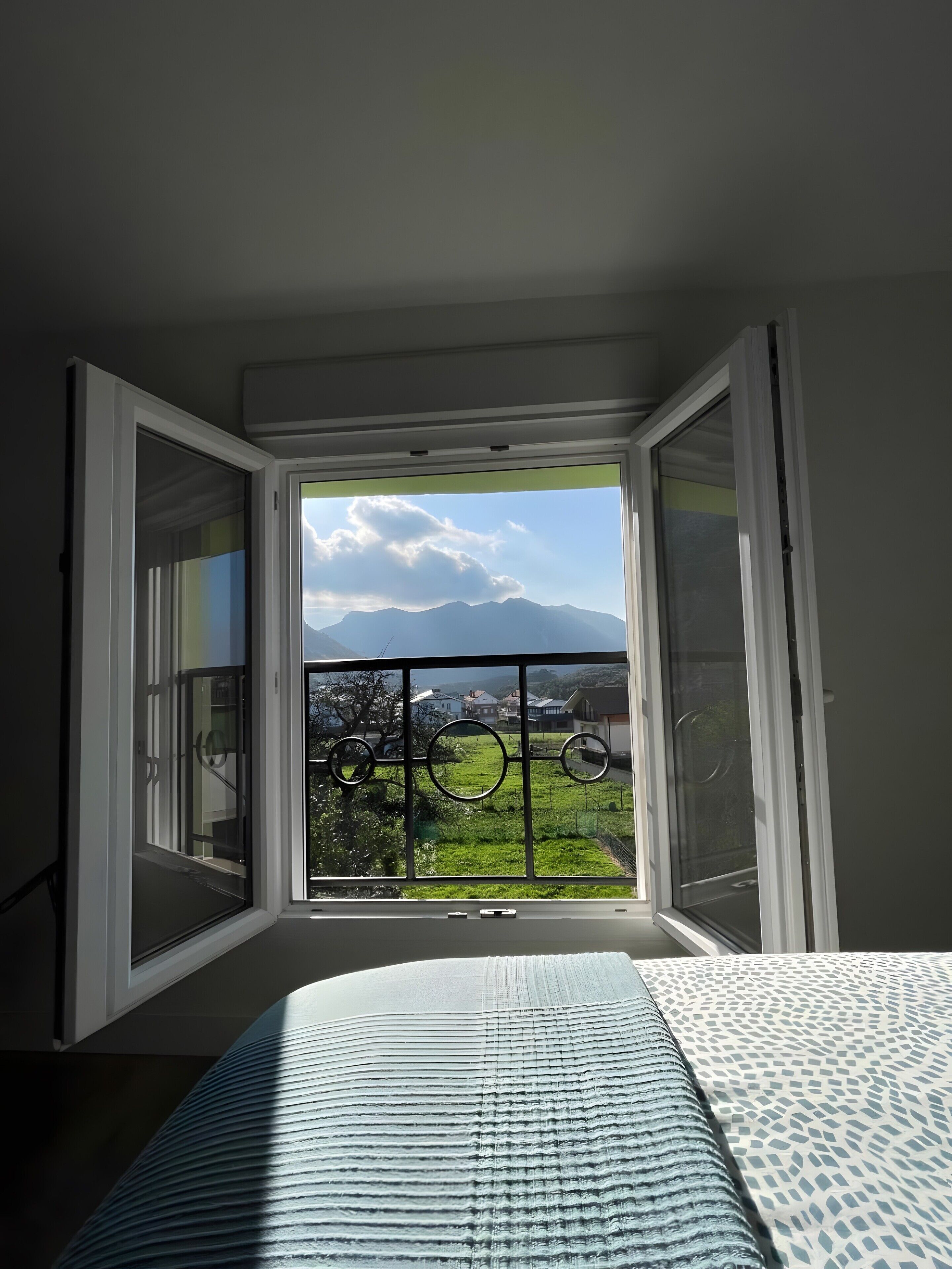 A room with a large window, a bed, and a view of a mountain and greenery.