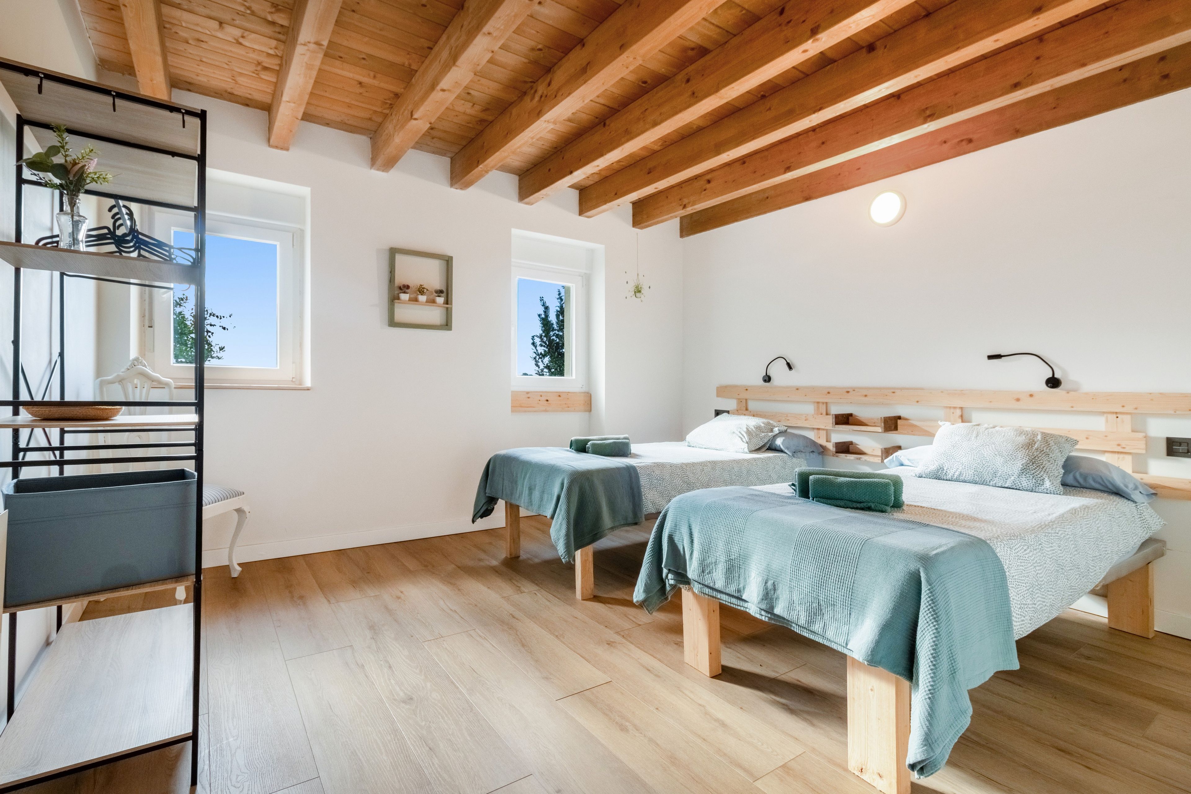 Een kamer met twee bedden, houten vloeren, een plank met planten en een raam.