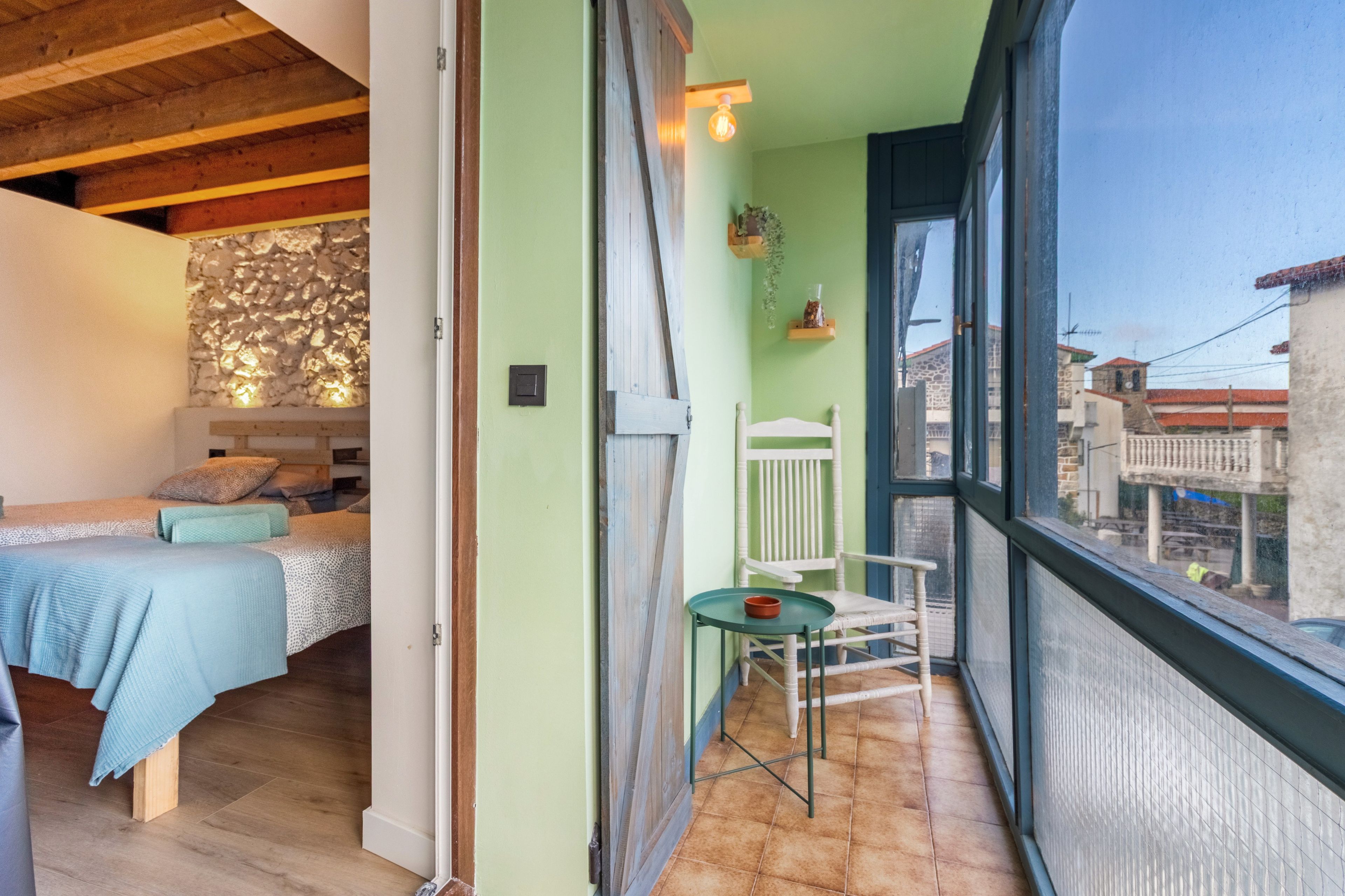 A room with a bed, a small table, a chair, and a view of the outside.
