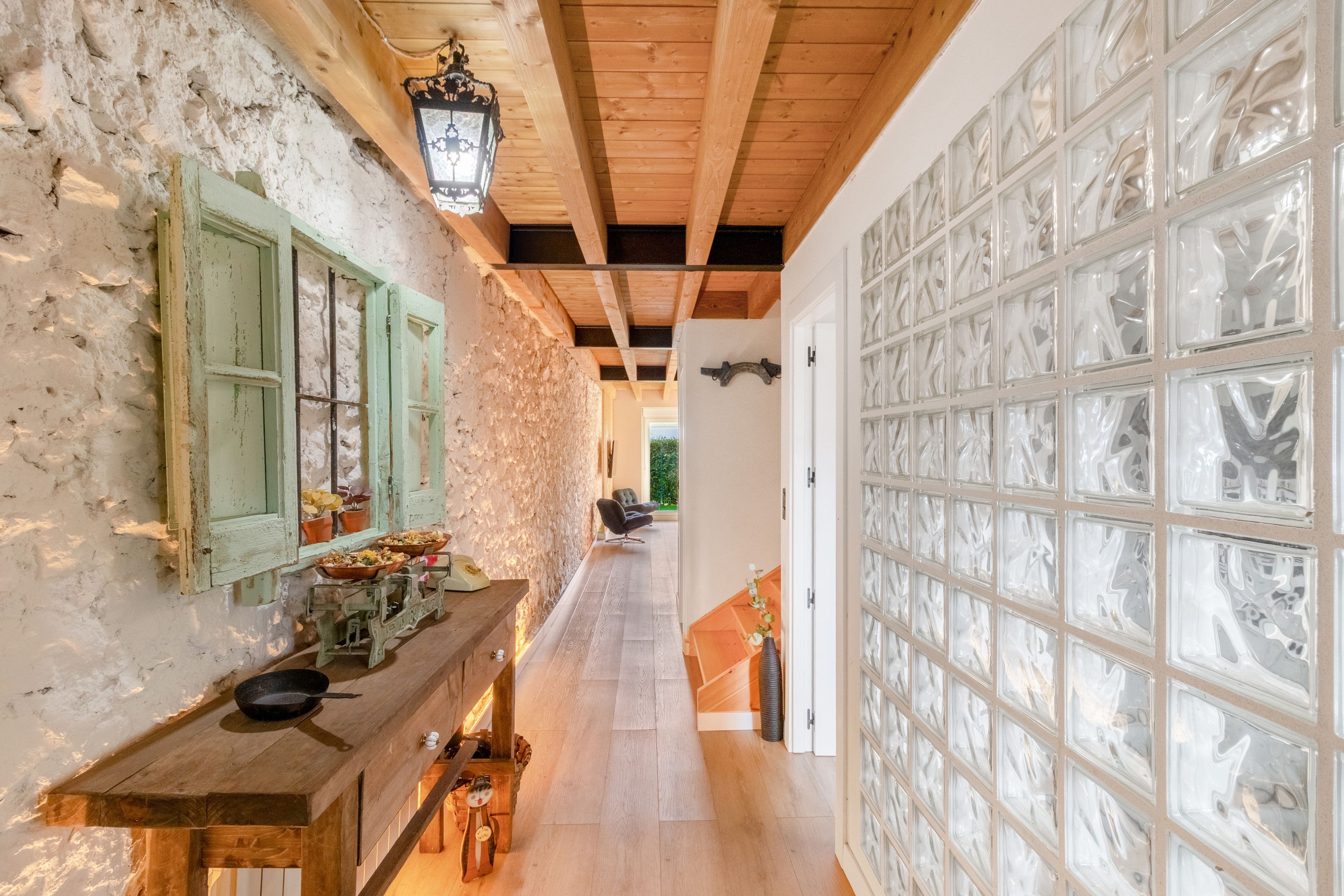 Un pasillo estrecho con techo de madera rústica, una pared de piedra en un lado y una puerta de cristal en el otro.