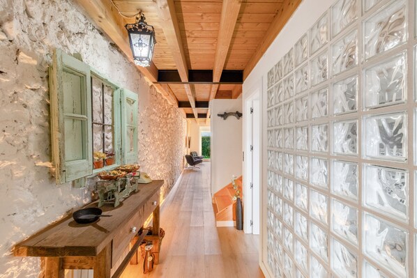 A narrow hallway with a rustic wooden ceiling, a stone wall on one side, and a glass door on the other.