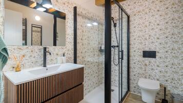 Un baño con tocador de madera, cabina de ducha con vidrio y un inodoro.