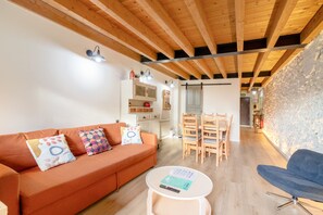 A modern living room with a wooden ceiling, a sofa with colorful cushions, a dining table with chairs, and a kitchen area in the background. - Holiday Home 'Verde & Mar' with Sea Views, Private Garden and Wi-Fi (Islares)