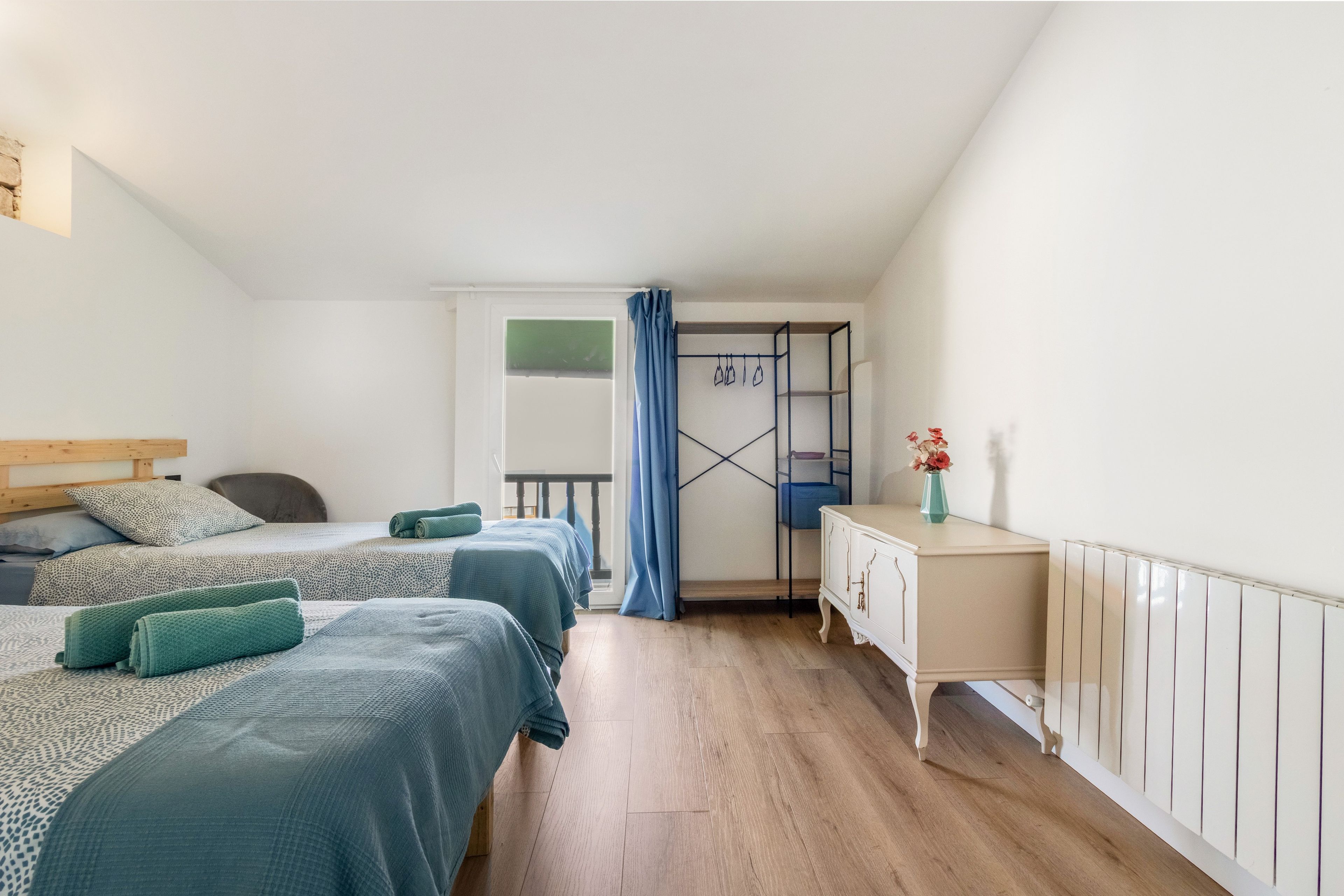 Un dormitorio con dos camas, un aparador, una ventana con cortinas y un balcón.