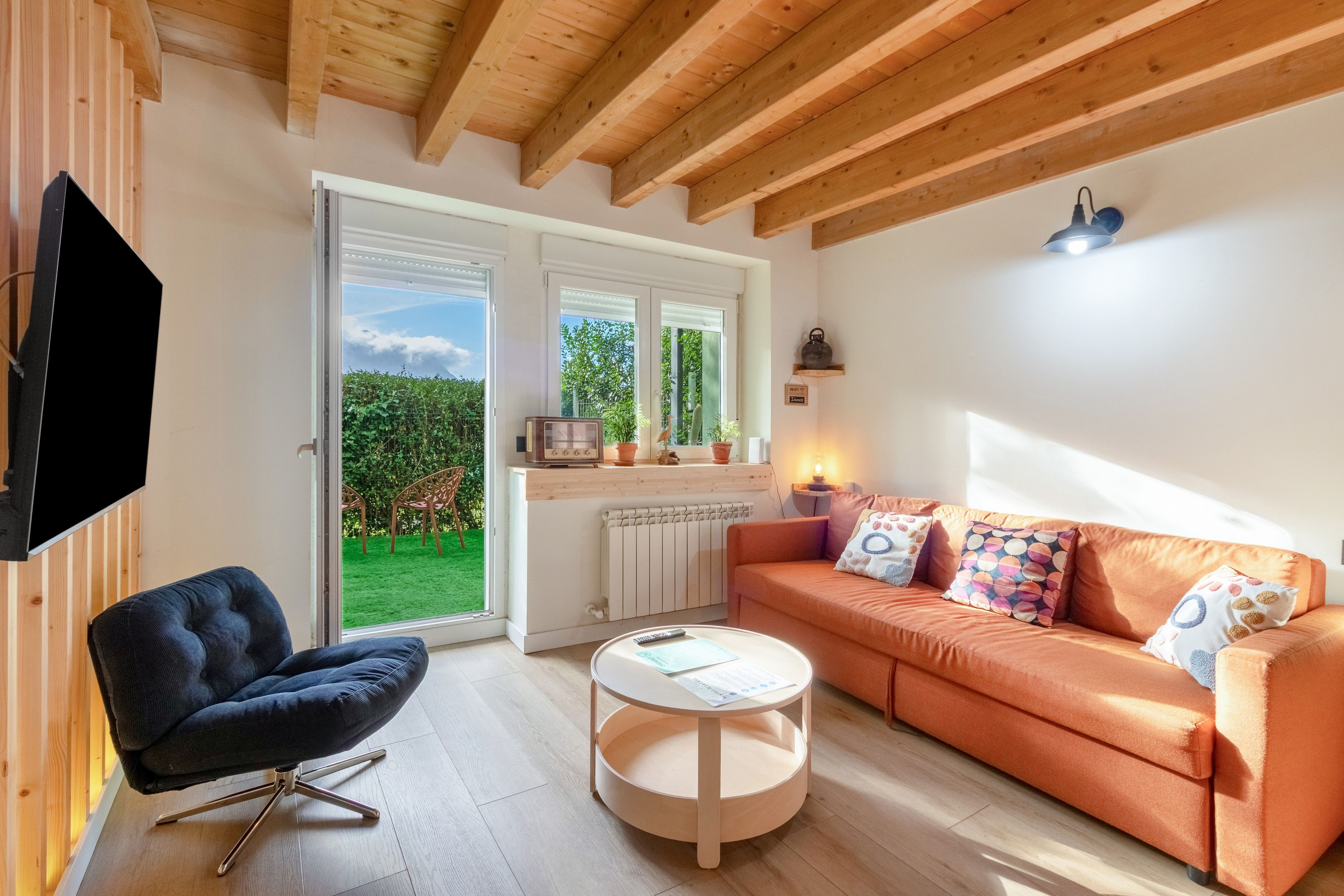 Una sala de estar moderna con un sofá, una silla, un televisor y una ventana con vistas a un jardín.