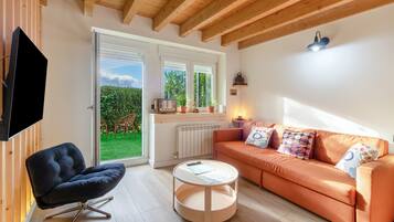 Una sala de estar moderna con un sofá, una silla, un televisor y una ventana con vistas a un jardín.
