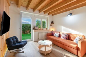 A modern living room with a sofa, a chair, a television, and a window overlooking a garden.