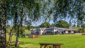 A large building with multiple rooms, a grassy field, and picnic tables. - 2 Bed in Usk- (oc-82391) (Kemeys Commander)