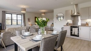A modern kitchen with a built-in oven, a dining area with a table set for four, and a living area with a sofa and a large window. - 2 Bed in Usk- (oc-82391) (Kemeys Commander)