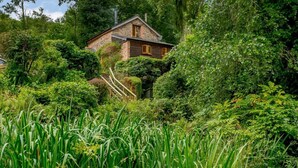 Ein rustikales Steinhaus, umgeben von dichtem Grün und hohem Gras.