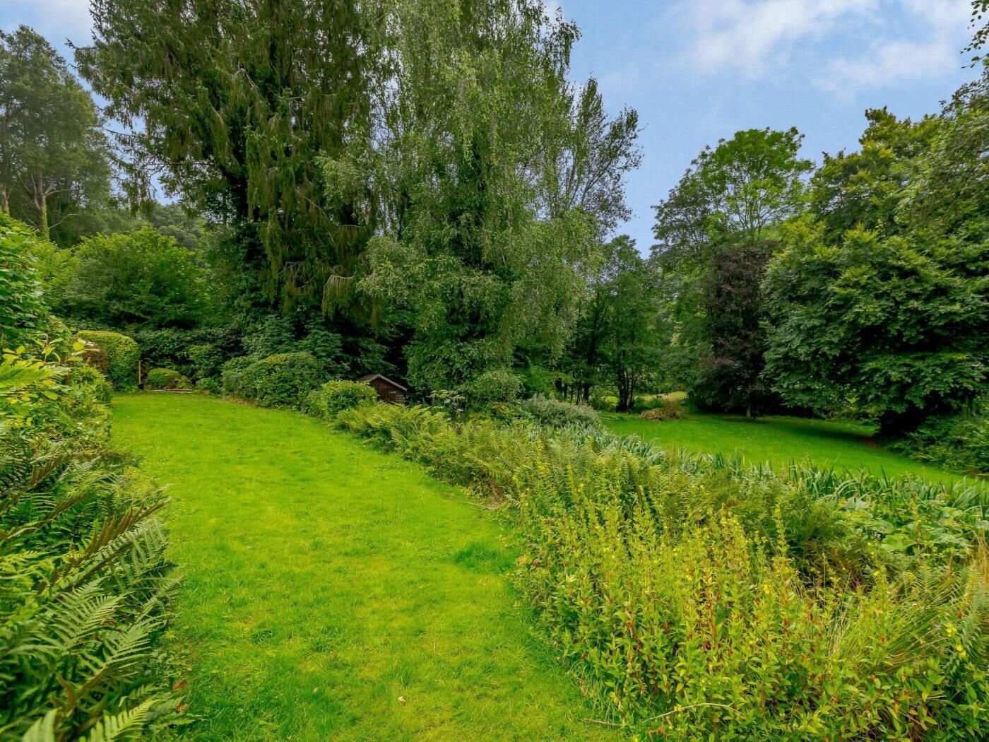 A lush garden with a variety of trees and shrubs, a well-maintained lawn, and a small wooden structure.