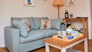 Ein Wohnzimmer mit einer Couch, einem Holztisch, Wandlampen und gerahmten Kunstwerken.
