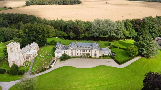 Ein weitläufiges Anwesen mit einem schlösserartigen Gebäude, großen, grünen Rasenflächen und einem Feld.