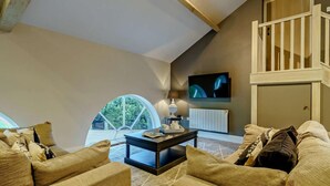 Ein geräumiges Wohnzimmer mit hoher Decke, einem großen Fenster, einem Fernseher und einer Treppe.