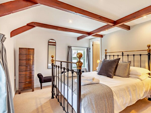 Ein Schlafzimmer mit Bett, Kommode, Sessel, Spiegel und Fenster.