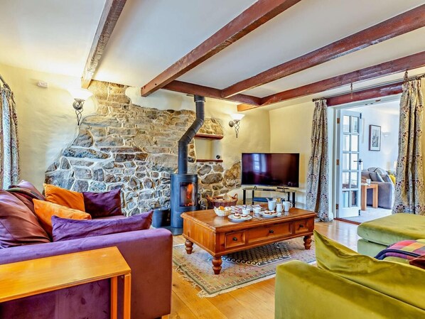 A cozy living room with a stone fireplace, wooden beams, a television, and comfortable seating. - 3 Bed in St. Columb (oc-82405) (Ruthvoes)