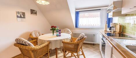 A dining area with a round table, wicker chairs, a hanging light fixture, and a window with curtains.
