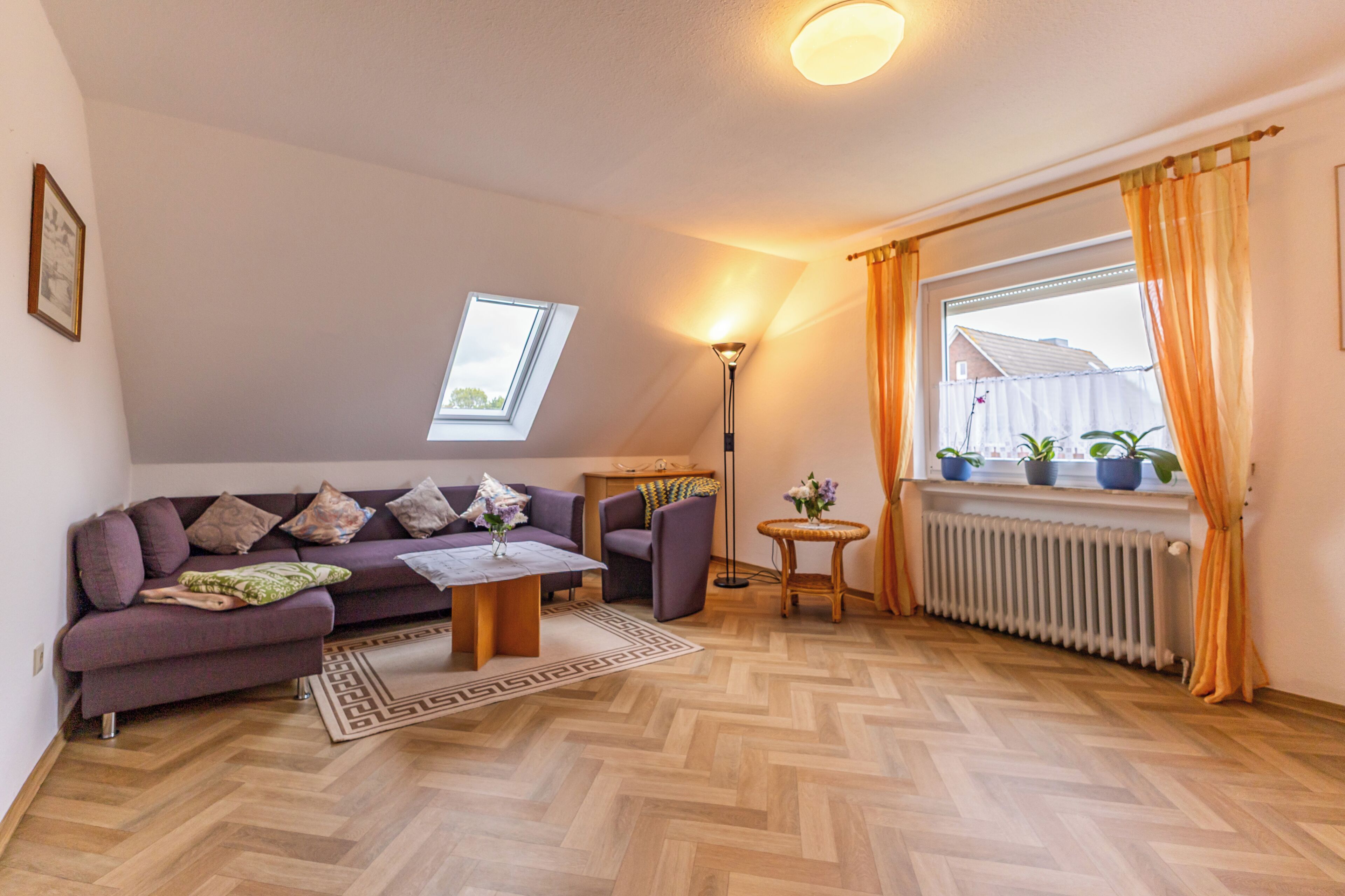 Un salon chaleureux avec un canapé, une table basse, une lampe, une petite table ronde agrémentée de plantes et une vue sur l’extérieur par une fenêtre.
