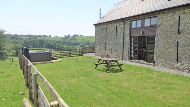A stone building with a fenced yard, a picnic table, and a view of the countryside. - 6 Bed in Llandovery (oc-82441) (Llanfair-ar-y-Bryn)
