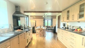 A spacious kitchen with wooden flooring, a central island, and a dining area with a sofa and table. - 6 Bed in Llandovery (oc-82441) (Llanfair-ar-y-Bryn)
