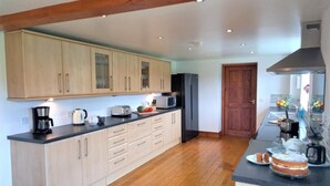 A modern kitchen with wooden cabinets, a central island, and a dining area with a table and chairs. - 6 Bed in Llandovery (oc-82441) (Llanfair-ar-y-Bryn)