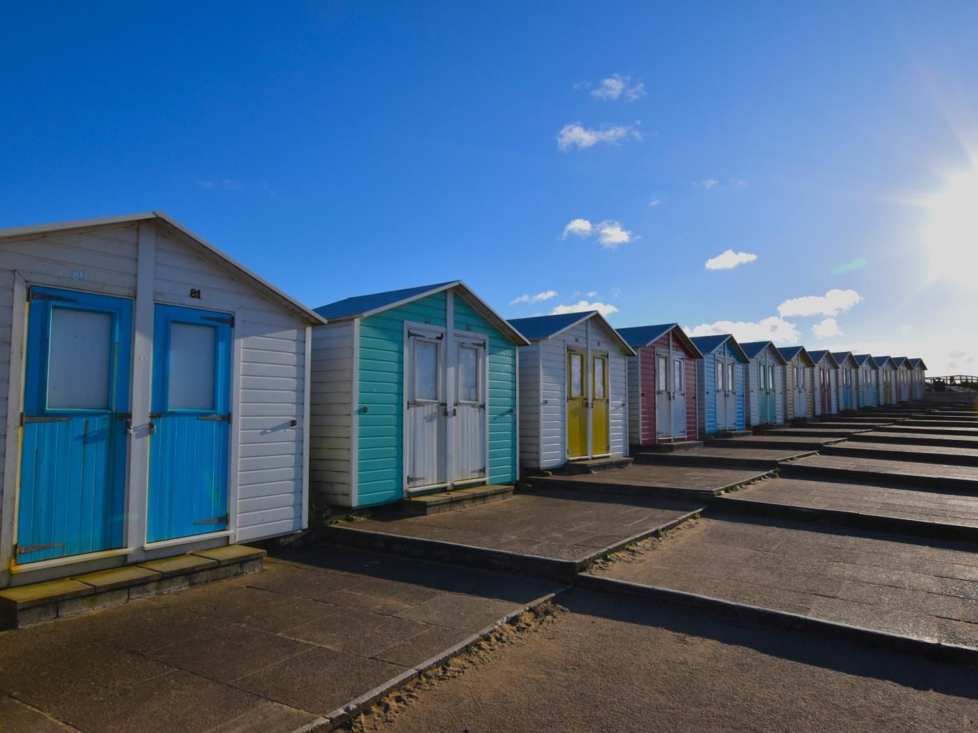 A row of beach huts with a clear sky and a sunlit path leading to them.