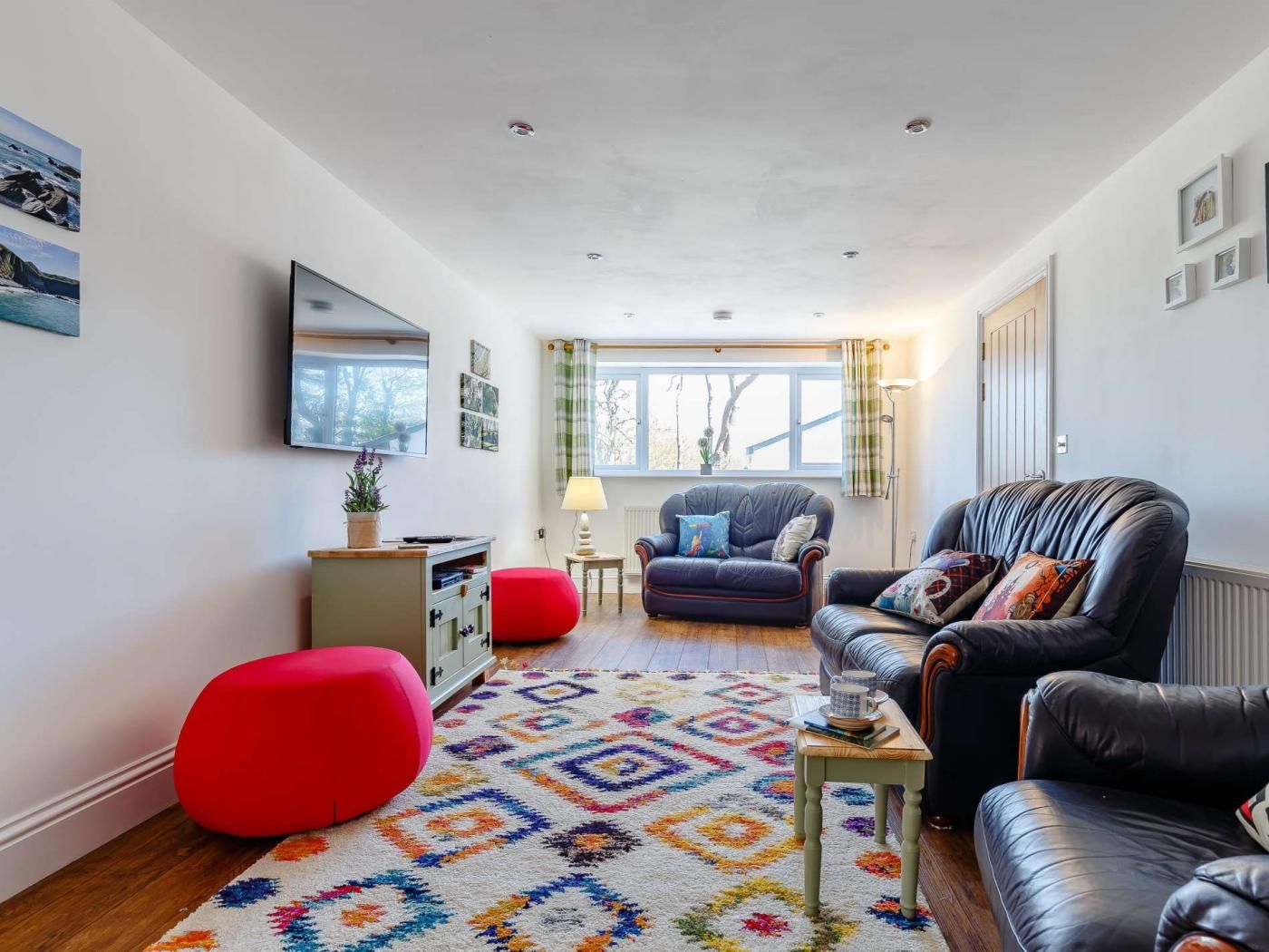 A modern living room with a sofa, armchairs, a red ottoman, a coffee table, and a patterned rug.