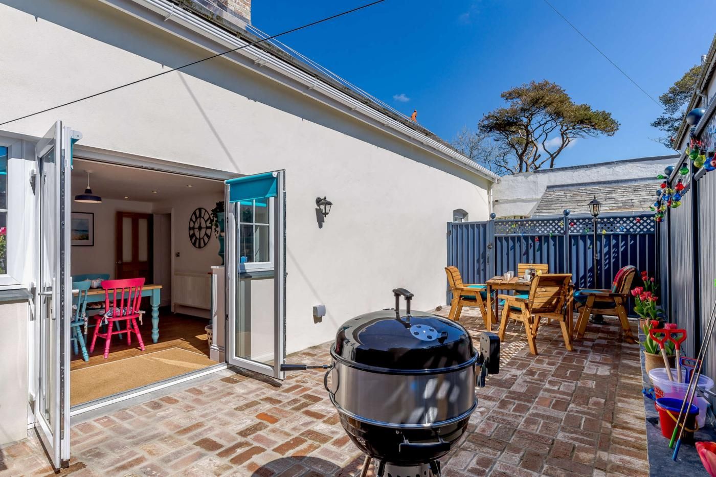 Une terrasse avec un barbecue, une table à manger avec des chaises et un portail bleu.