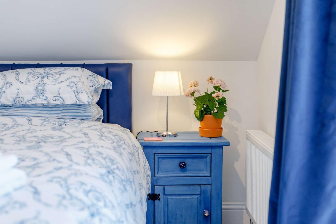 Une chambre à coucher avec un lit, une table de chevet, une lampe et une plante en pot.