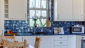 Una cocina con armarios blancos, encimera negra, microondas y ventana con vistas a árboles.
