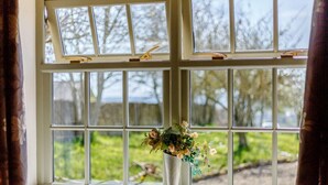 Una ventana con vistas a la vegetación y un florero con flores en el alféizar.