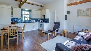 Una cocina moderna con armarios blancos, un salpicadero azul y un comedor con mesa y sillas de madera.